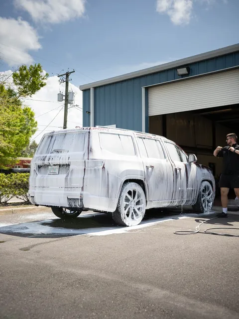 An SUV covered in foam outside the open bay door, full sun