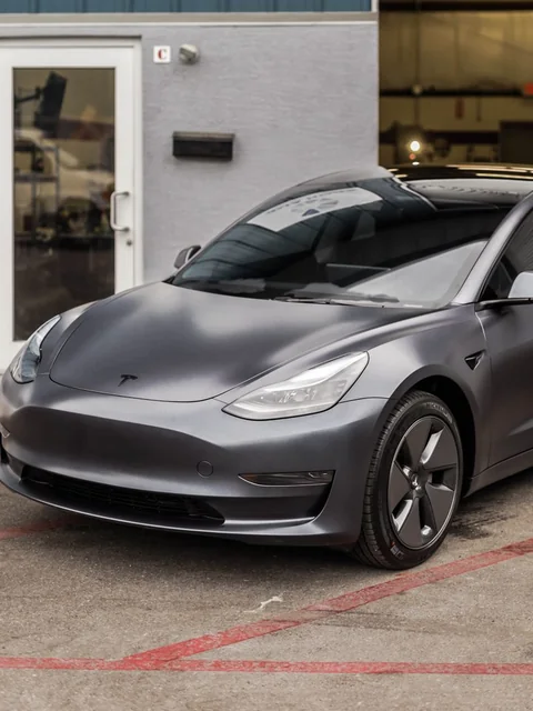 A matte grey sedan parked outside an open bay door