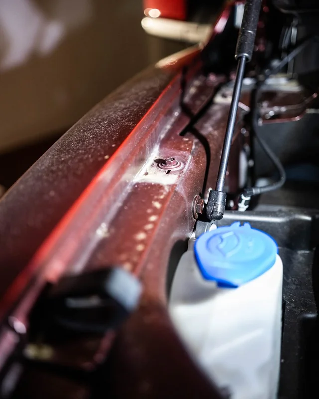A hood strut over a fluid bottle, under a red hood