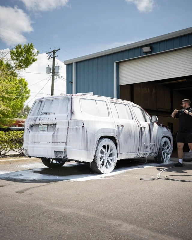 An SUV covered in foam outside the open bay door, full sun